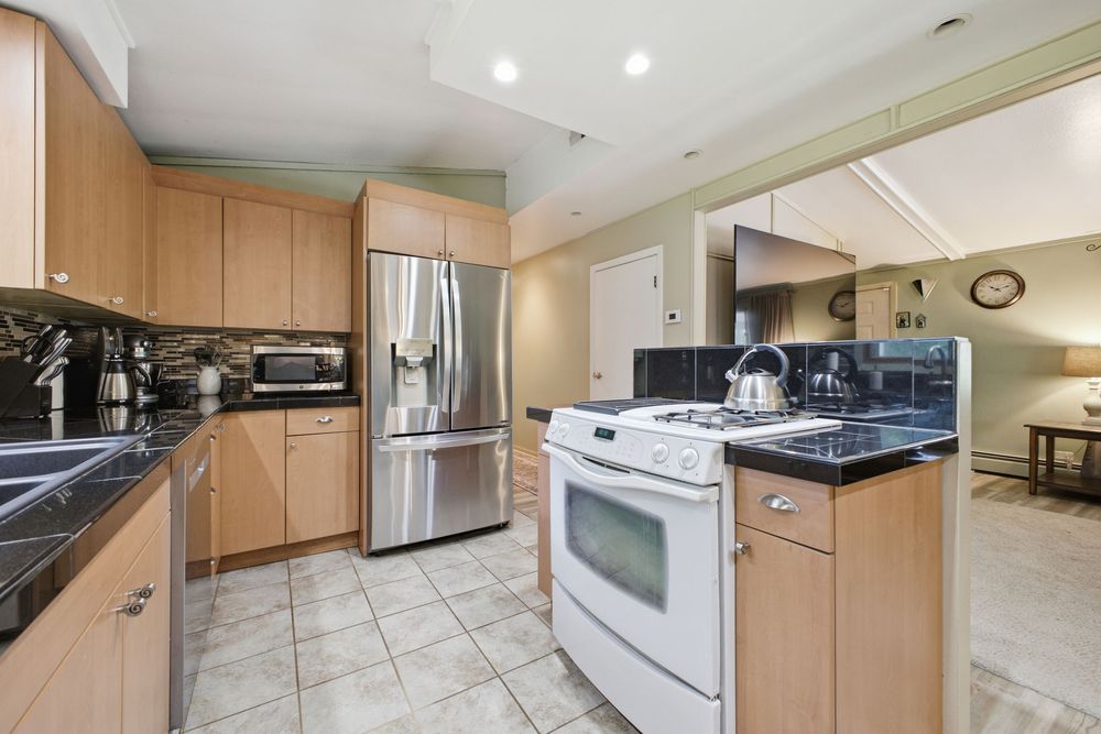 Modern kitchen featuring light maple cabinets, stainless steel refrigerator, white gas range, and dark granite countertops.