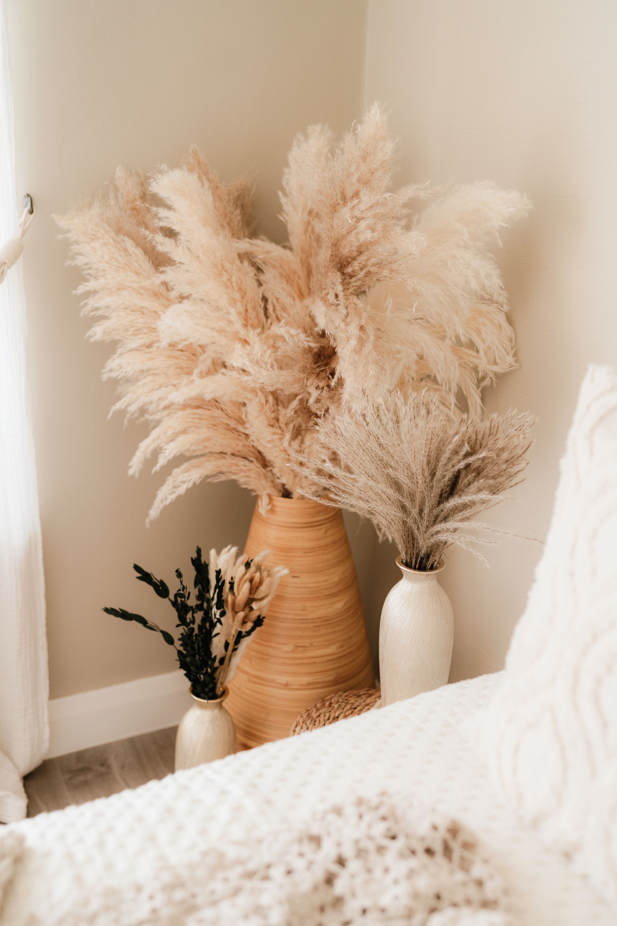 Boho bedroom corner with pampas grass in terracotta and white vases against a neutral wall.