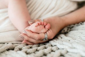 A mother gently holds her newborn baby's tiny feet in her hands on a soft knit blanket.