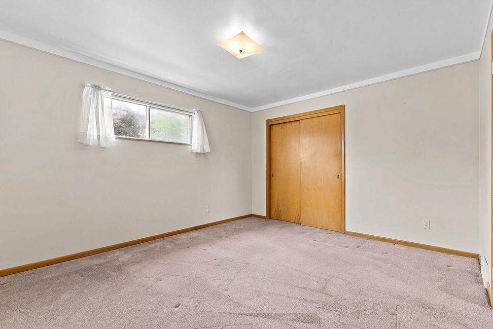 Empty bedroom with beige carpet, crown molding, closet door, and single window with natural light.