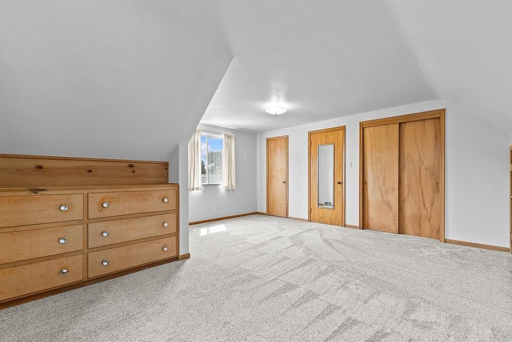 Spacious attic bedroom with vaulted ceiling, built-in wood dresser, neutral carpet, and two closets with wood doors.