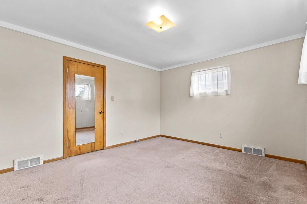 Empty bedroom with neutral carpet, crown molding, two windows, and visible closet with wooden door.