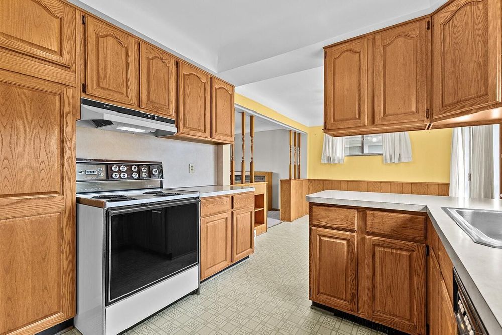 Oak kitchen cabinets with white electric range, light countertops, and vinyl flooring in a bright traditional kitchen.