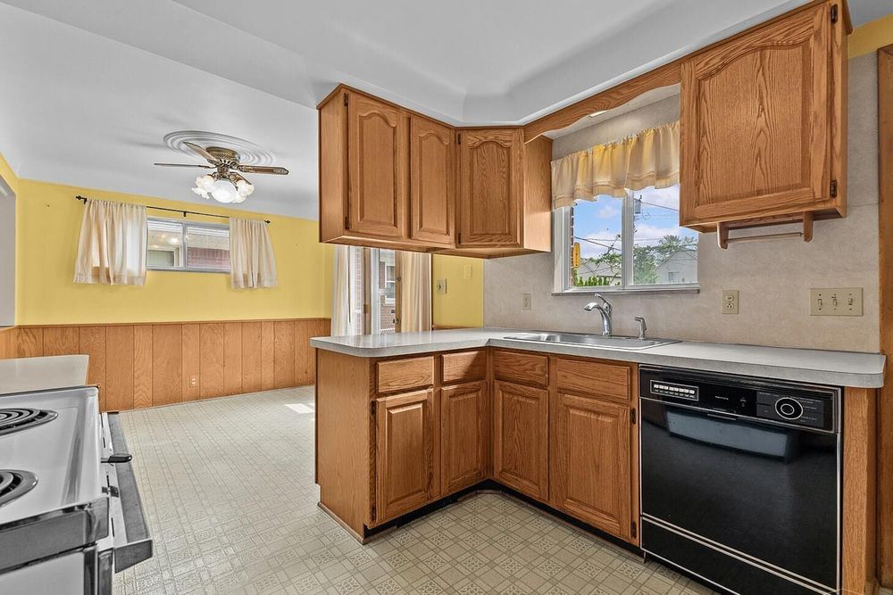 Kitchen with oak cabinets, black dishwasher, double sink, vinyl flooring, and yellow walls with wood paneling accents.