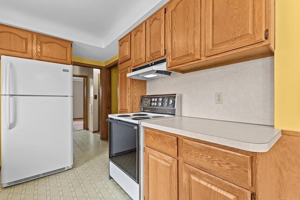 Kitchen with oak cabinets, white refrigerator, electric stove, and light countertops on vinyl flooring.