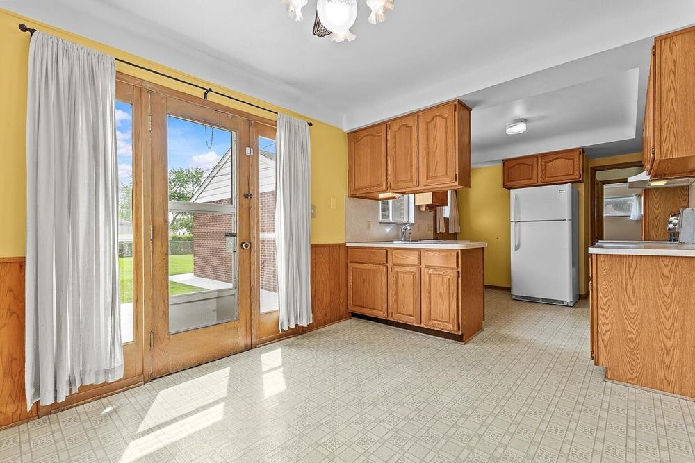 Bright kitchen with oak cabinets, white refrigerator, French doors leading to backyard, and vinyl tile flooring.