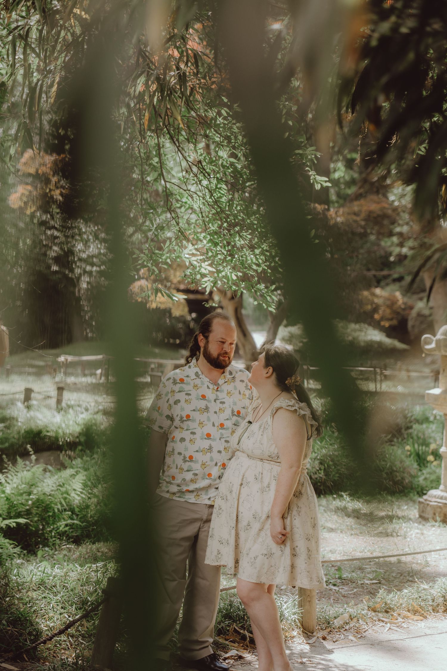 Couple sharing a romantic moment in a lush garden, framed by hanging green branches in soft natural light.