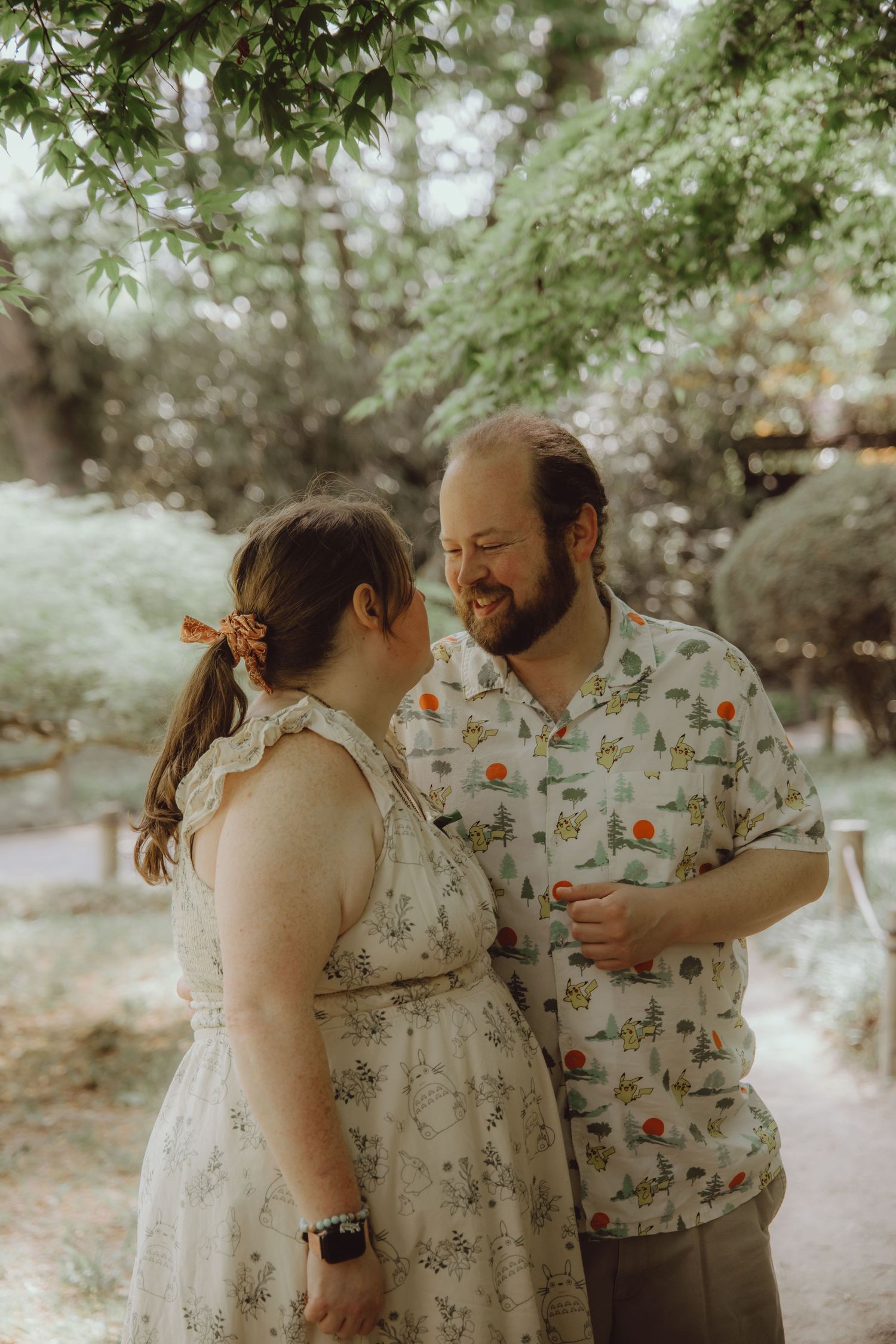 A couple shares a joyful moment in a lush garden, wearing floral outfits, smiling warmly at each other.