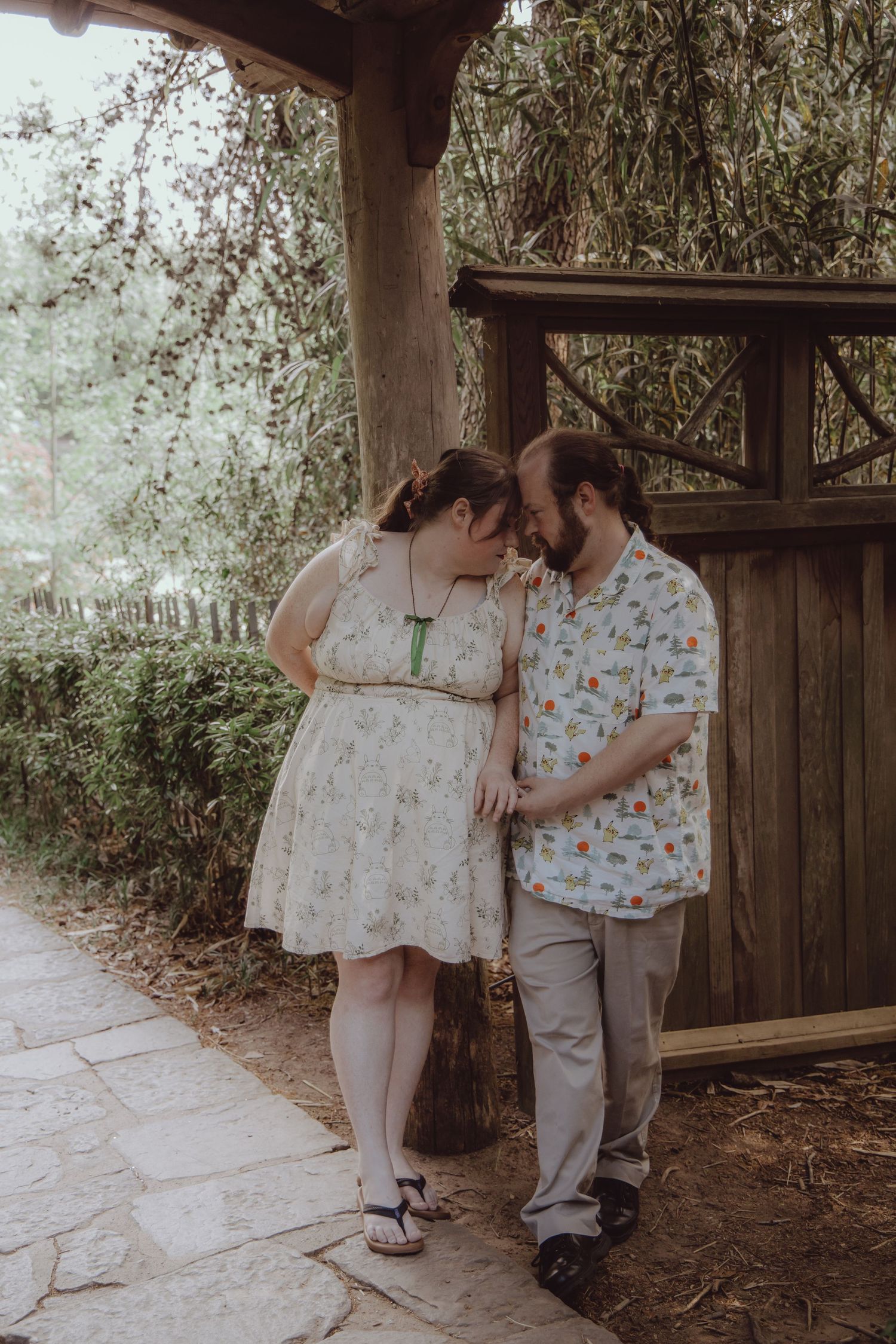 Couple sharing a romantic moment touching foreheads near a wooden gate surrounded by lush greenery.