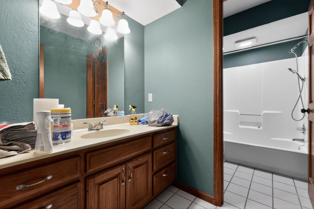 Bathroom with wood cabinets, large vanity mirror, single sink, and a white bathtub-shower combo on teal painted walls.