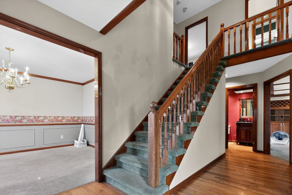 Elegant foyer with carpeted staircase, wood banisters, hardwood floors, chandelier, and decorative wallpaper border in a classic home.