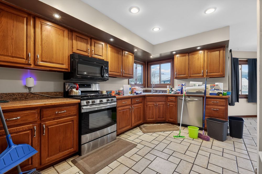 Spacious kitchen with rich brown cabinetry, stainless steel appliances, granite countertops, and light tile flooring.