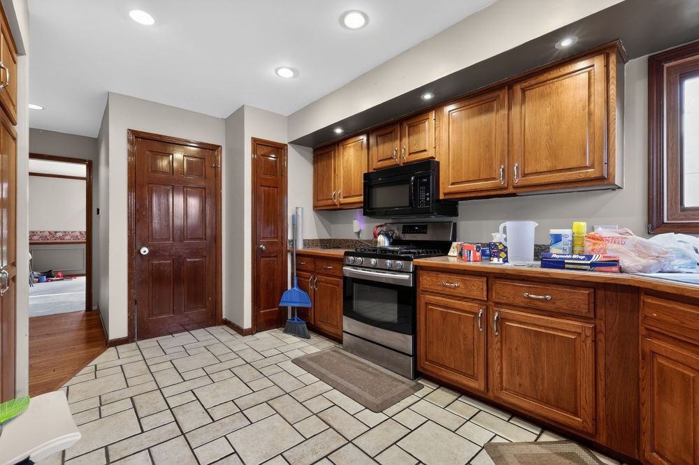 Kitchen with brown wood cabinets, stainless steel gas range, black microwave, and light tile flooring.