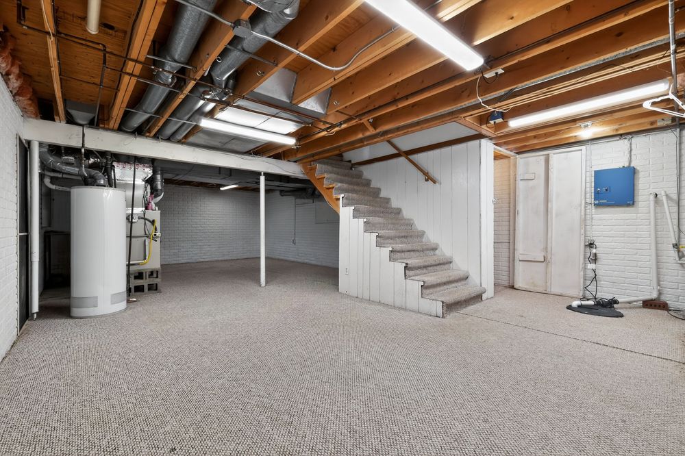Unfinished basement with concrete stairs, water heater, exposed ceiling beams, and painted white walls with epoxy floor.