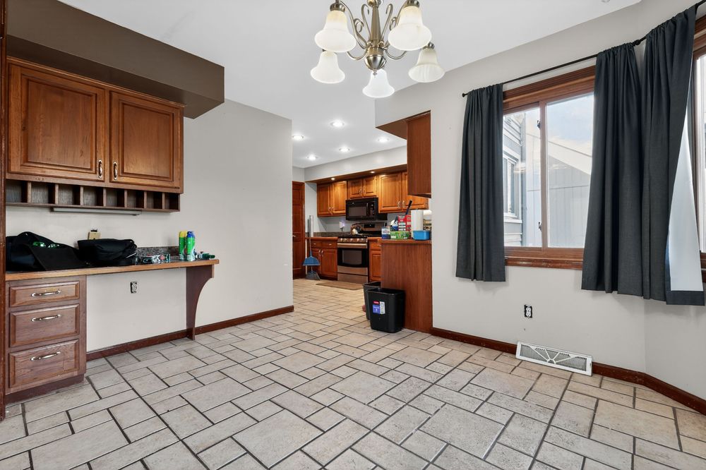 Open kitchen and dining area with wood cabinets, tile flooring, chandelier, and black appliances in a bright home.