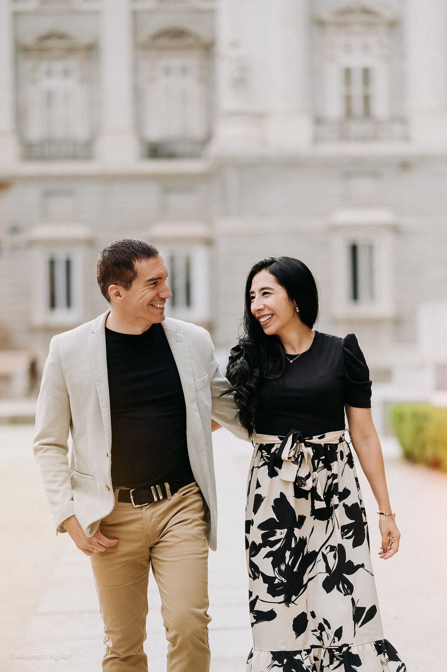 Smiling couple walking together in front of a grand white building in Madrid.