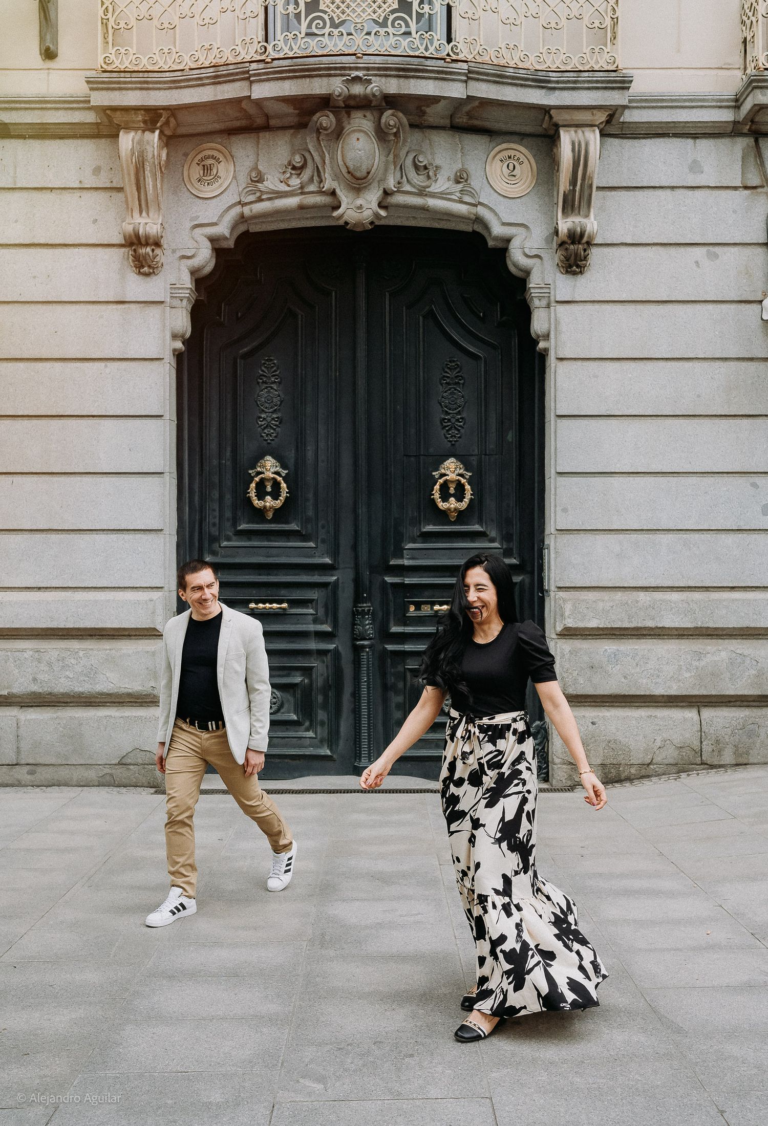Couple walking hand in hand in front of ornate green doors of a historic building.