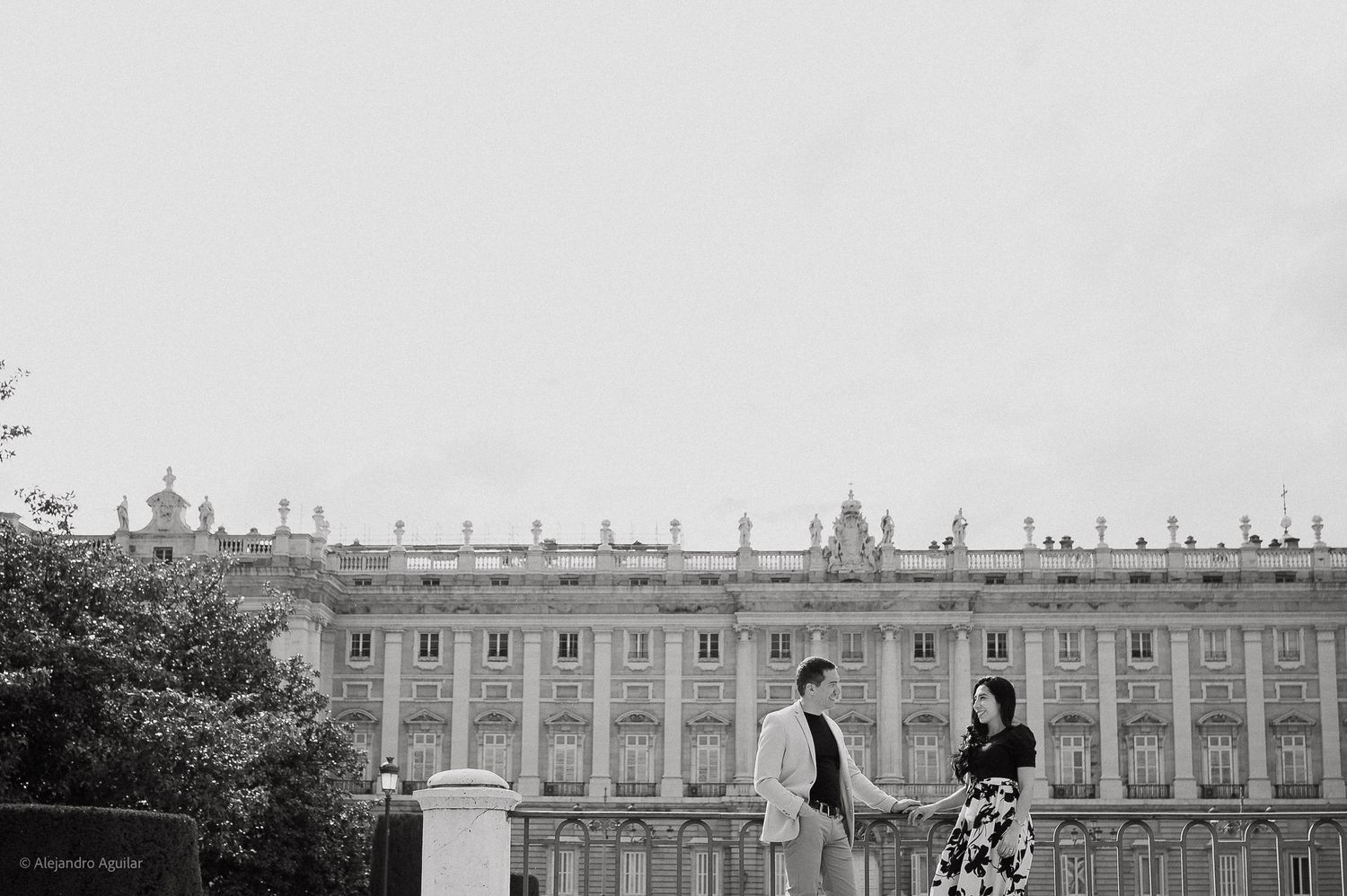 Black and white photo of couple standing before the Royal Palace of Madrid.