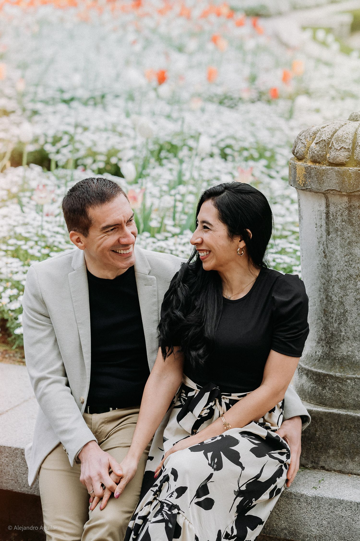 Happy couple sitting together on stone steps surrounded by colorful spring flowers.
