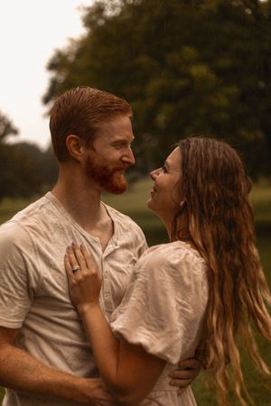 Romantic couple embracing in the rain, smiling at each other in a green outdoor setting.