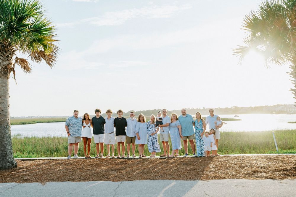 Large family group posing together near a palm tree overlooking a scenic coastal marsh landscape.