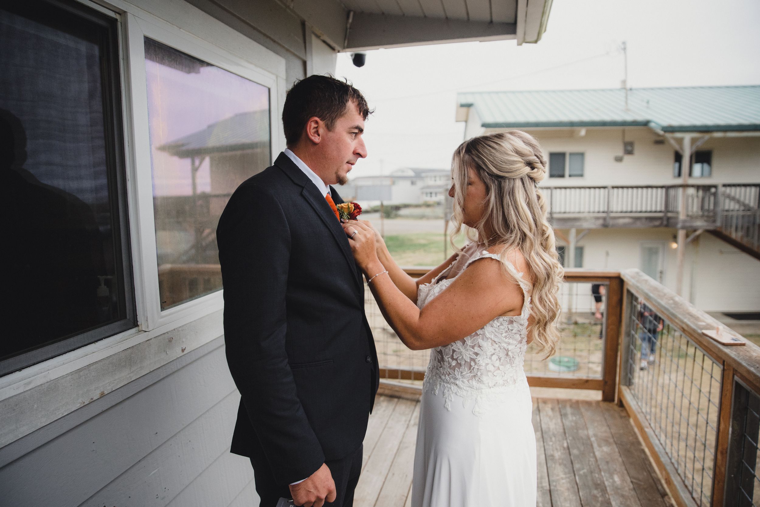 Bride adjusting groom boutonniere on outdoor deck before wedding ceremony.
