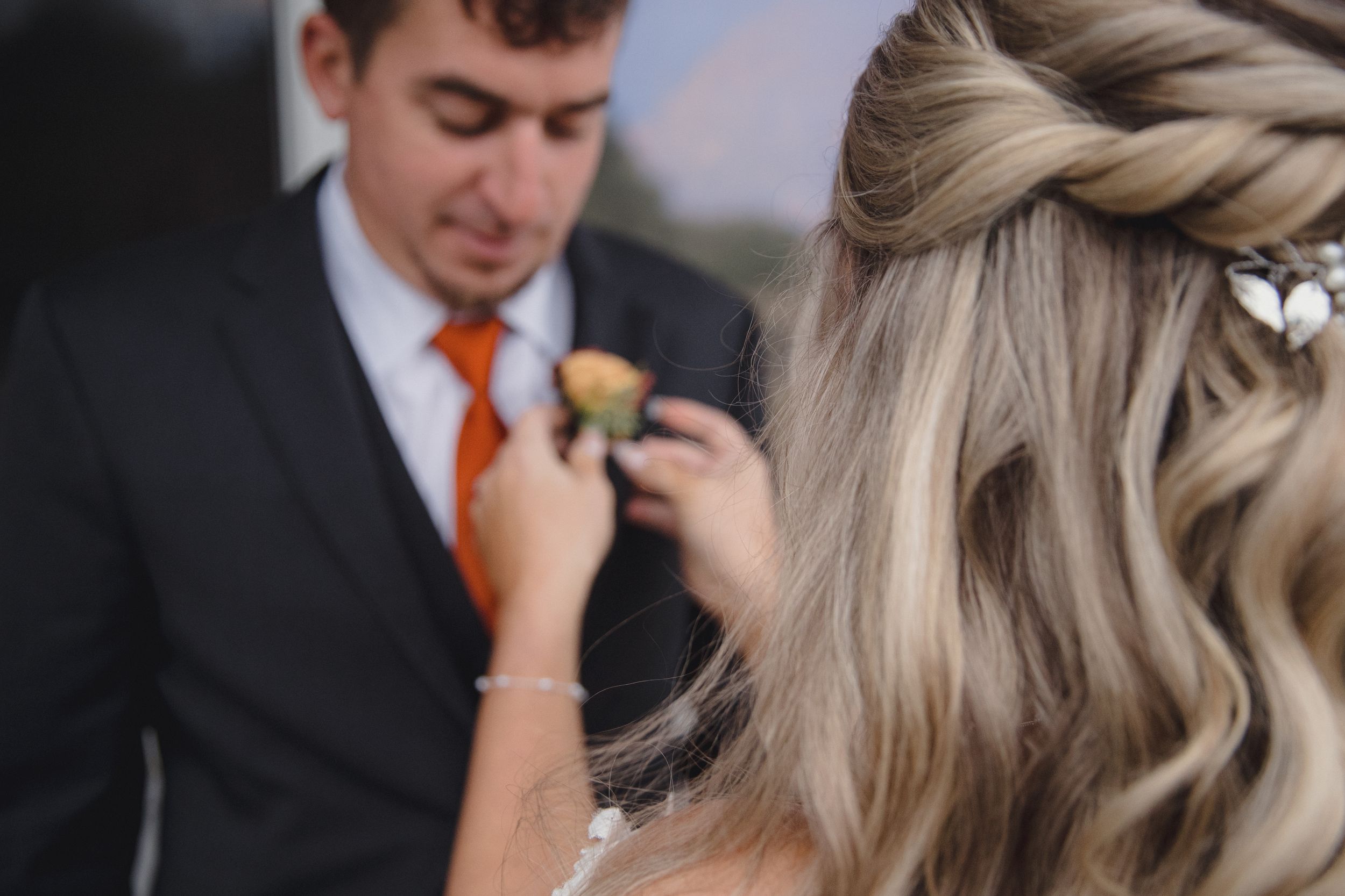 Bride pinning a boutonniere on groom in orange tie at wedding ceremony.
