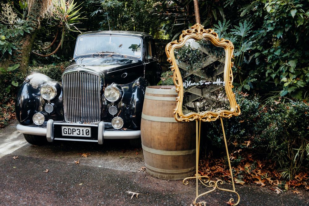 Vintage black Bentley classic car beside barrel and ornate gold mirror at wedding.
