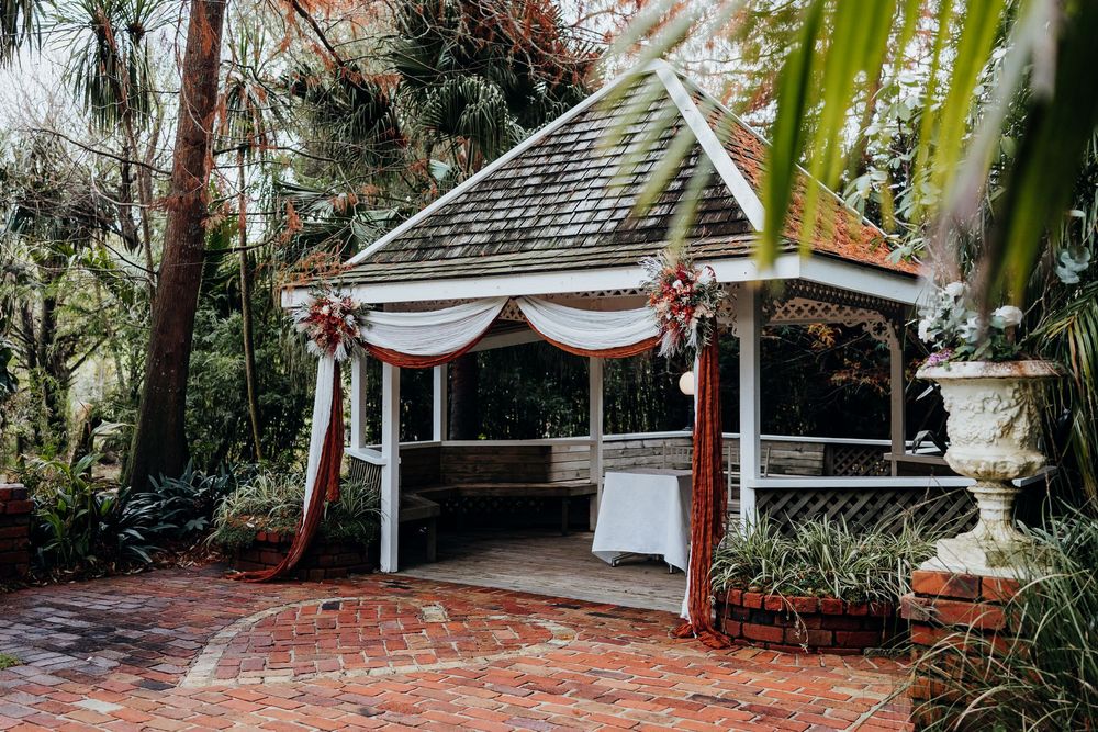 Elegant white gazebo decorated with floral arrangements and draped fabric in a lush garden wedding venue.