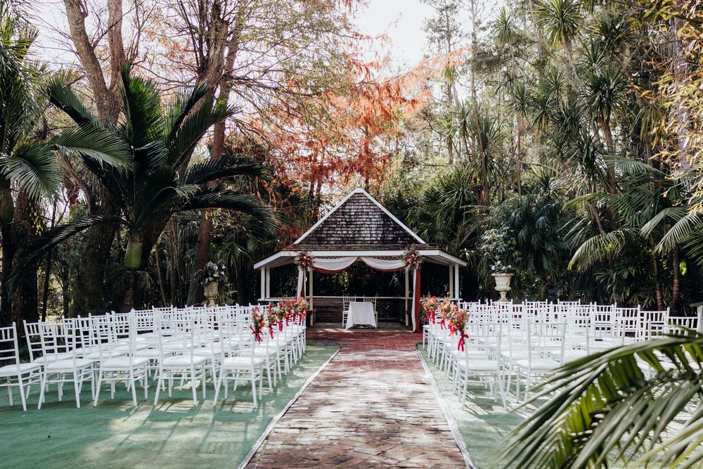 Outdoor wedding ceremony setup with white chairs and floral decor beneath a tropical garden gazebo.