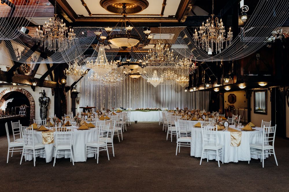 Elegant wedding reception hall with crystal chandeliers, white chiavari chairs, and gold table settings.