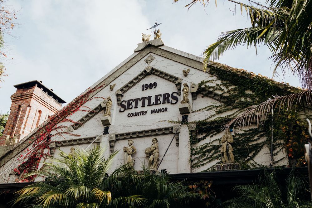 Settlers Country Manor wedding venue exterior with lush greenery and vintage signage dating back to 1909.
