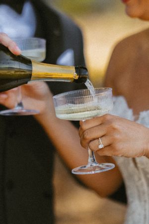 Champagne being poured into a coupe glass held by a bride wearing an engagement ring at a wedding reception.