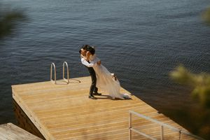 Bride and groom share romantic embrace on wooden dock overlooking calm blue lake waters on their wedding day.