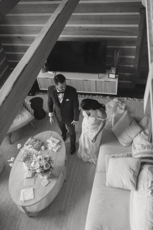 Aerial black and white photo of bride and groom in a rustic cabin living room with floral bouquet on coffee table.