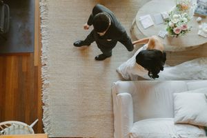 Aerial view of a couple in wedding attire standing near a white sofa and floral centerpiece on a neutral rug.
