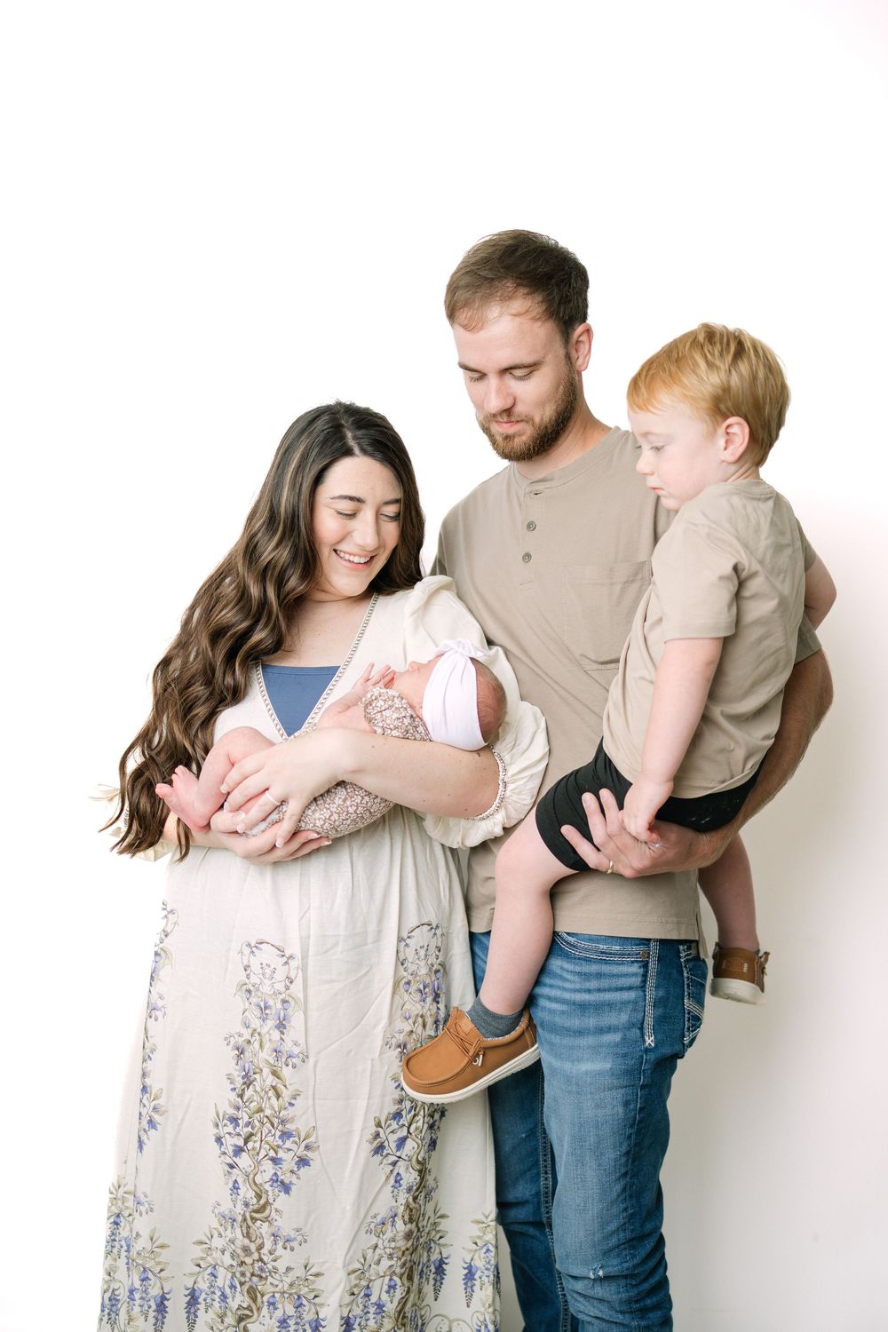 A young family with a newborn baby and toddler son poses together against a white background.