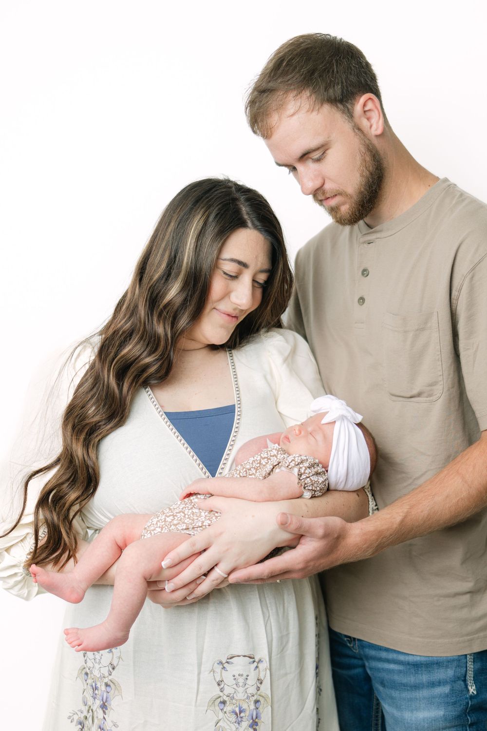 A couple tenderly gazes at their newborn baby against a white studio background.