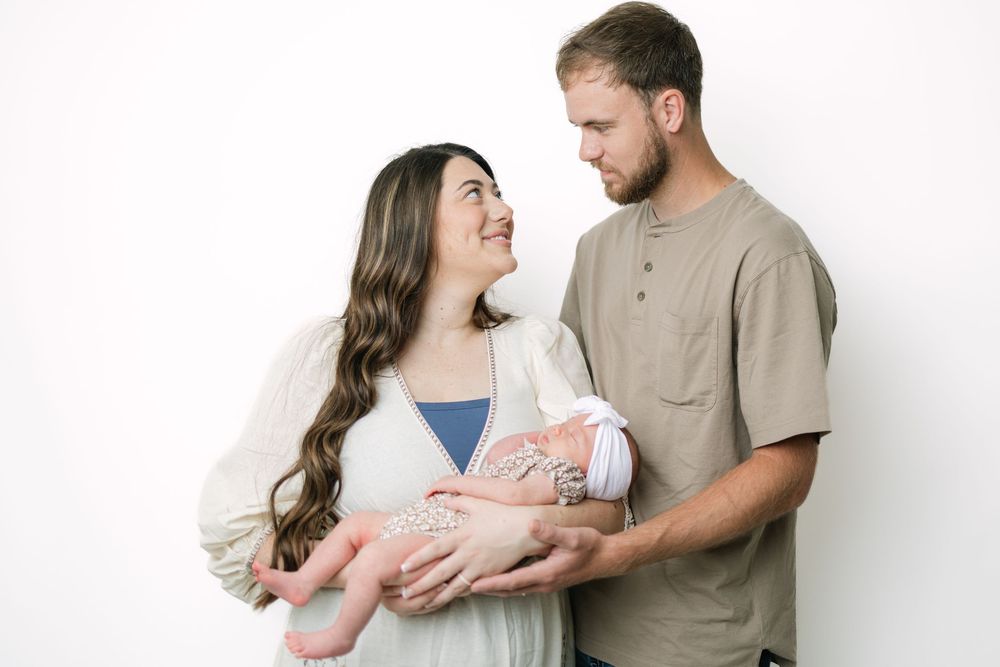 Happy couple smiling at each other while holding their newborn baby against a white background.