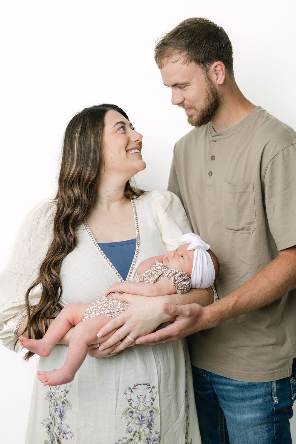 Smiling couple holding their newborn baby in a bright white studio during a professional newborn photography session.