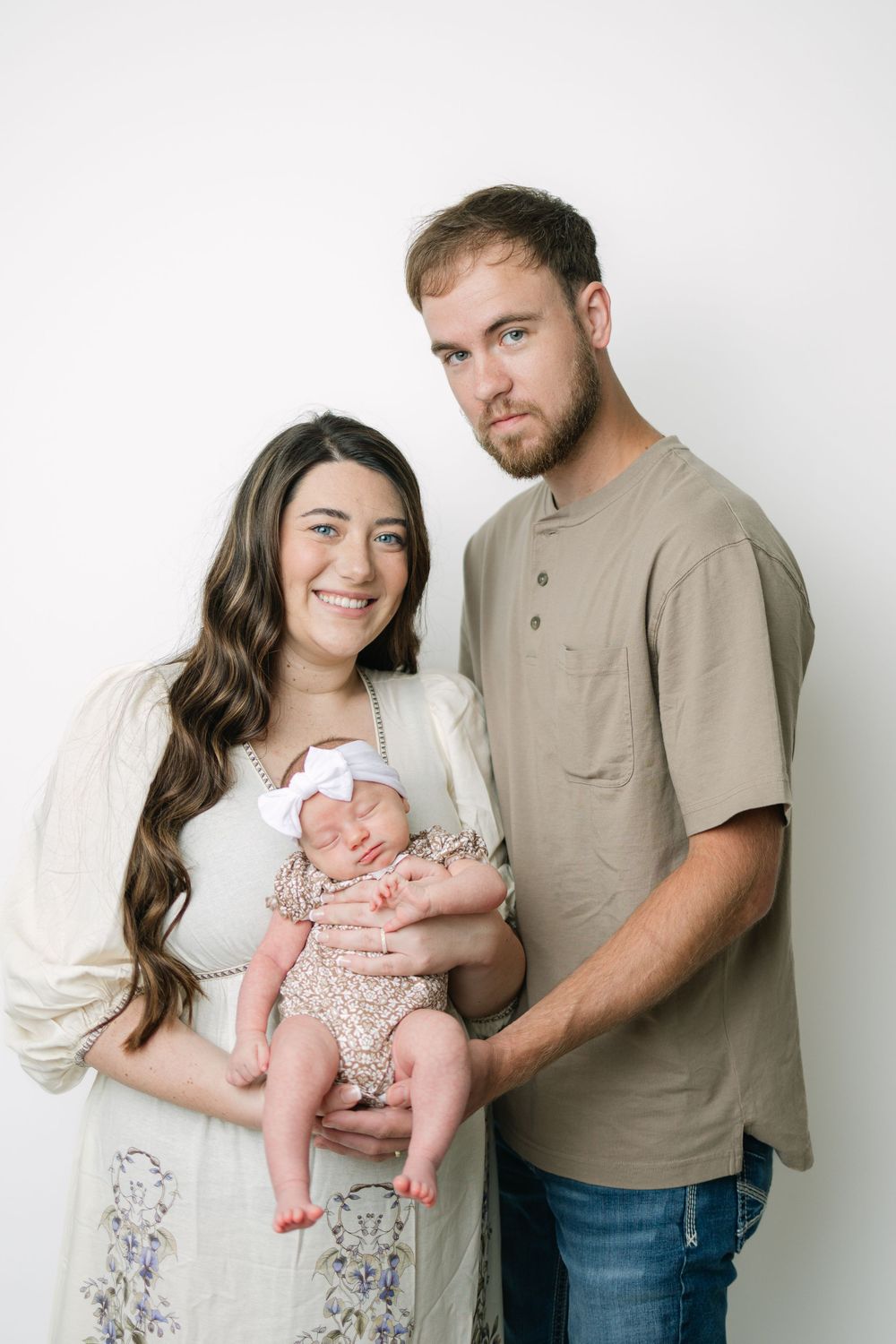 Young couple smiling and holding their newborn baby girl in a white studio portrait session.