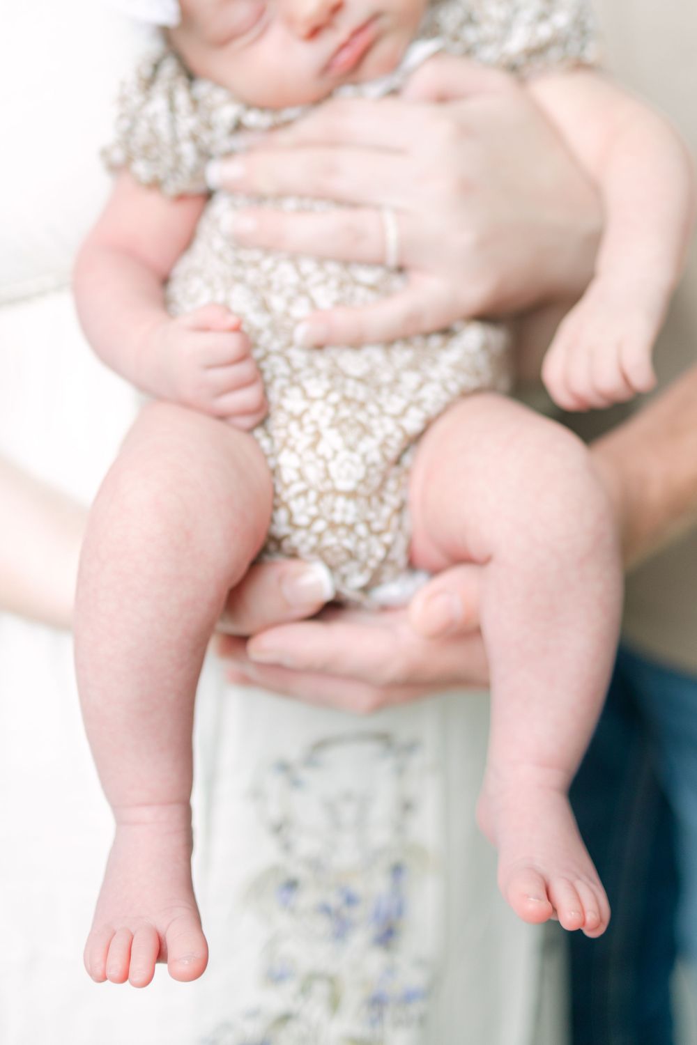 Close-up of a newborn baby's tiny feet and legs being cradled in parents' hands during a newborn photo session.