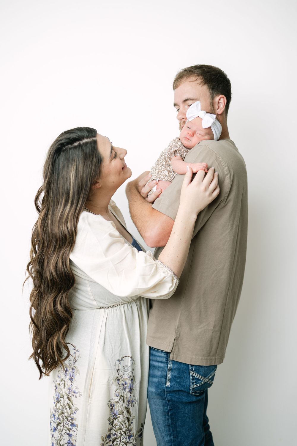 A couple shares a tender moment holding their newborn baby in a white studio setting.
