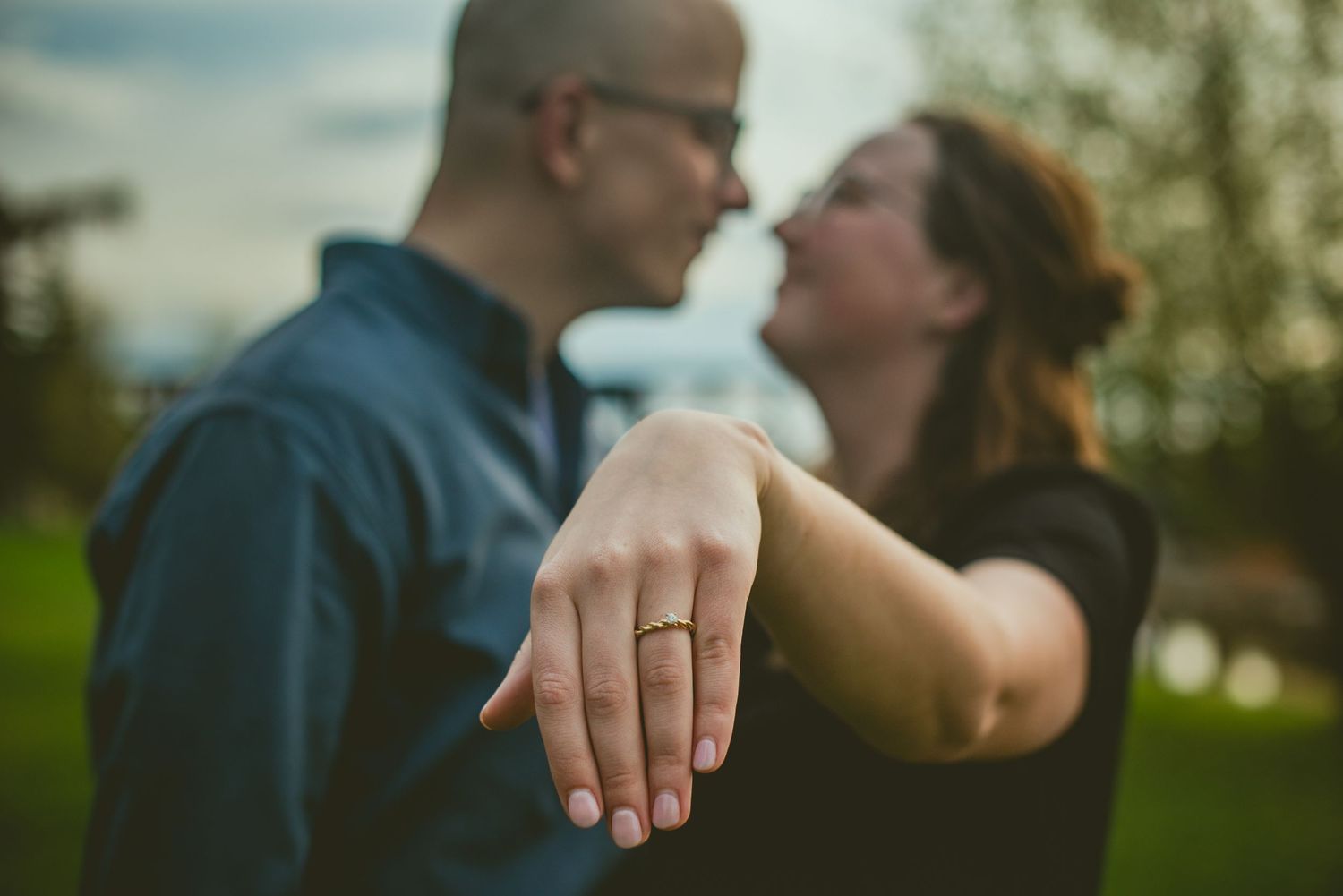 Engaged couple sharing a romantic moment while showing off engagement ring in outdoor setting.