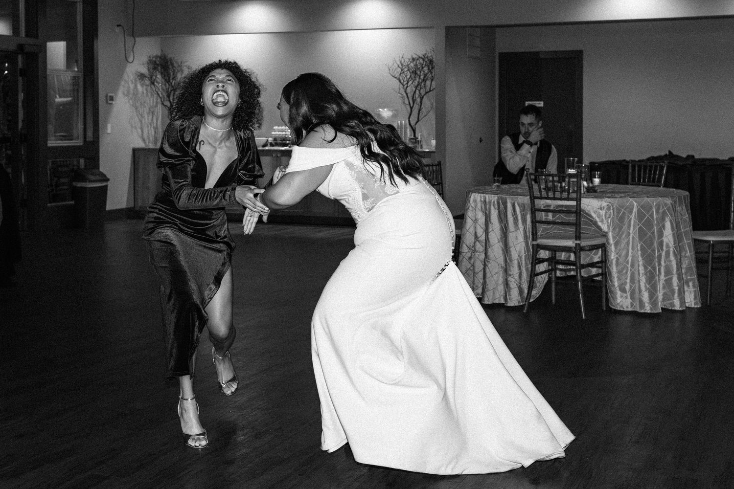 Bride and guest dancing energetically at wedding reception in black and white photo.