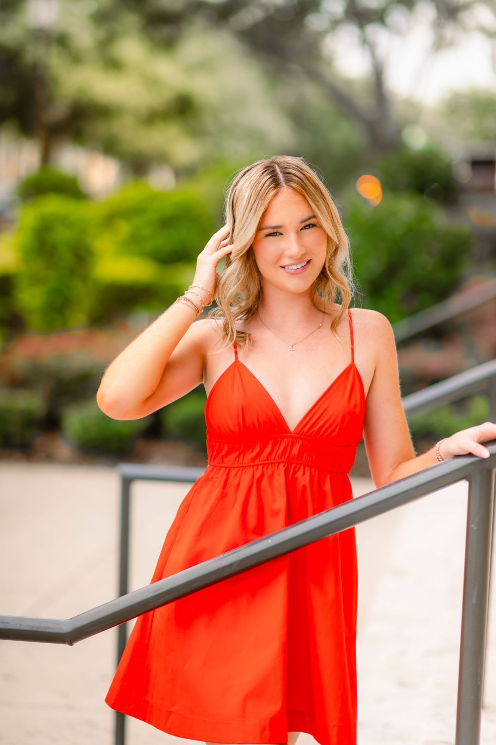 Smiling blonde woman in a red mini dress leaning on a railing outdoors.