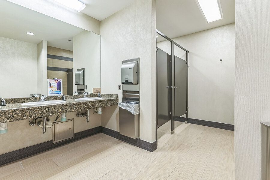 Clean commercial restroom with granite countertop vanity, large mirror, and private stall partitions.