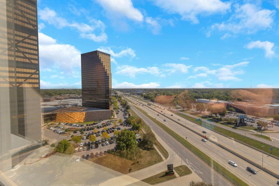 Aerial view of urban highway corridor flanked by tall office towers and commercial buildings under blue sky.