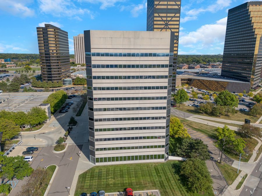 Aerial view of a modern multi-story office building surrounded by green landscaping and urban streets under a blue sky.
