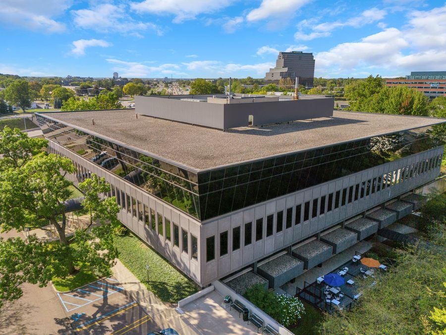 Aerial view of a modern glass and concrete office building surrounded by mature trees in an urban campus setting.